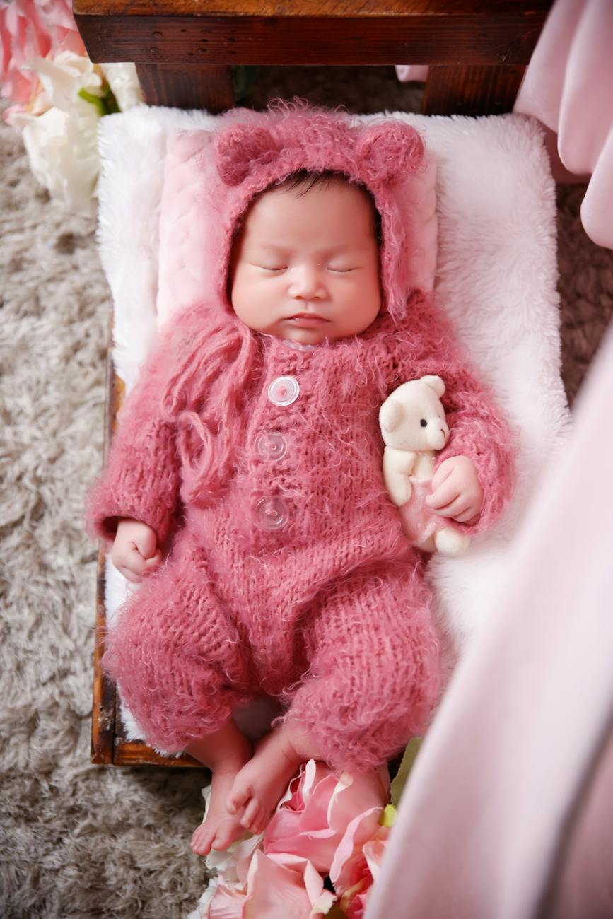 sleeping baby in red knitted romper holding a teddy bear