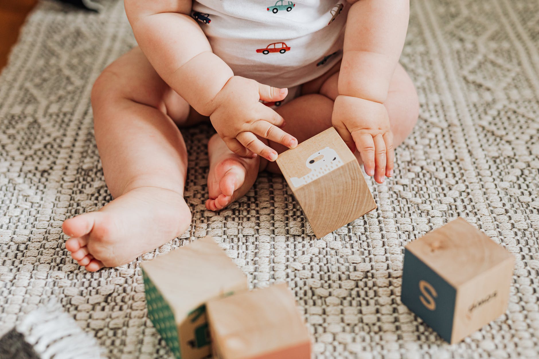 baby sitting on carpet playing with wooden toy blocks